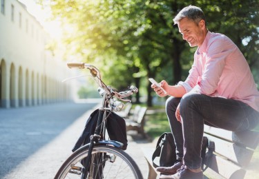 Smiling man with bicycle checking the phone on a park bench