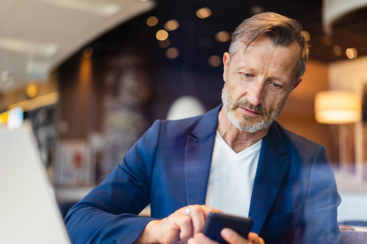 Mature businessman in blazer using smart phone at cafe