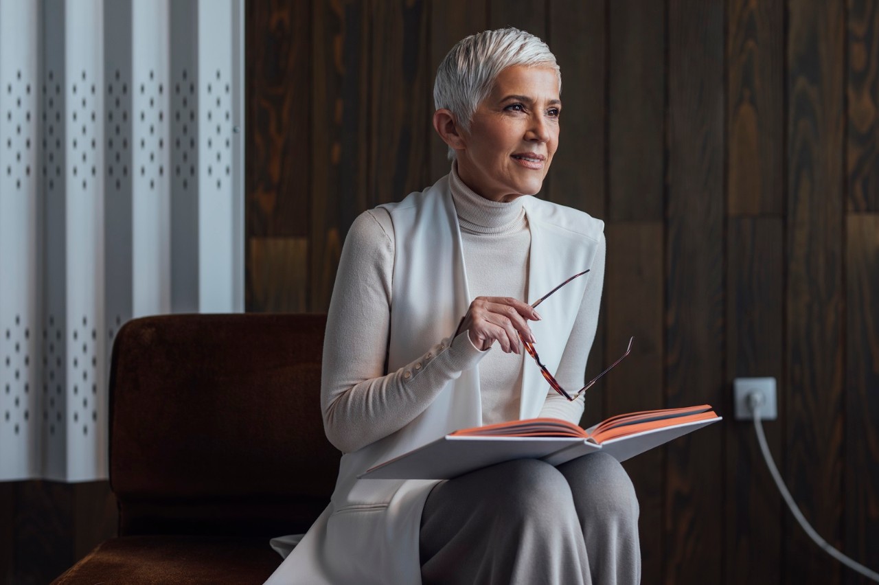 A beautiful senior woman sitting in her office and going through a furniture design catalogue.