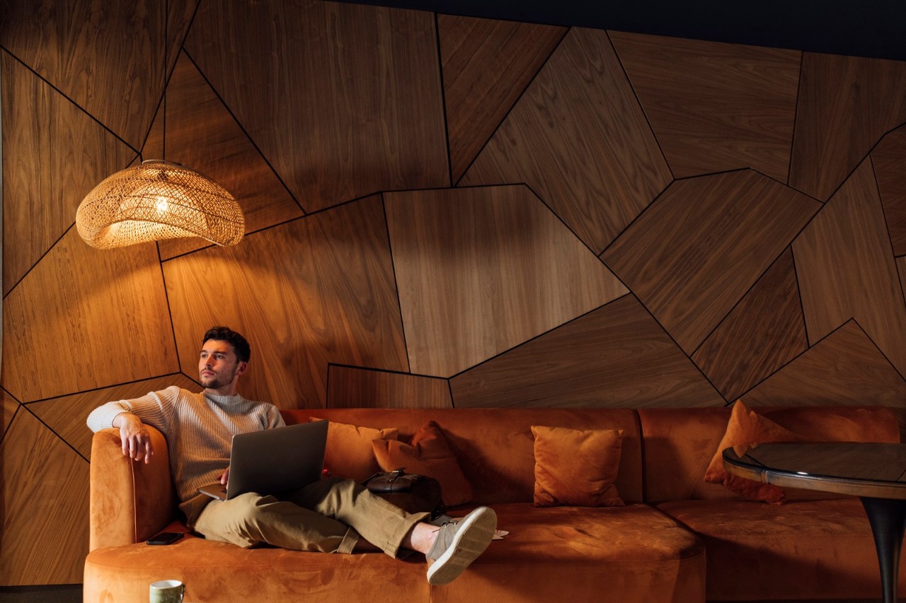 A young man on a staycation at Newton Hall in Northumberland, North East England. He is sitting on a plush sofa in the luxury holiday let he is staying in while using his laptop, doing some freelance work. He is taking a quick break and looking to his side at the view out the window.Videos also available for this scenario.