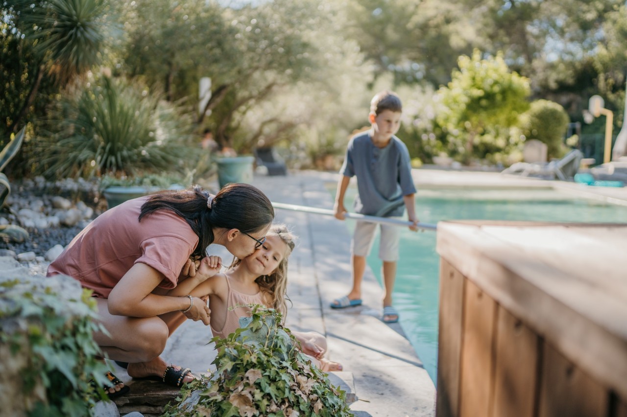 Mother and little daughter gardening while son cleaning outdoor swimming pool in backyard