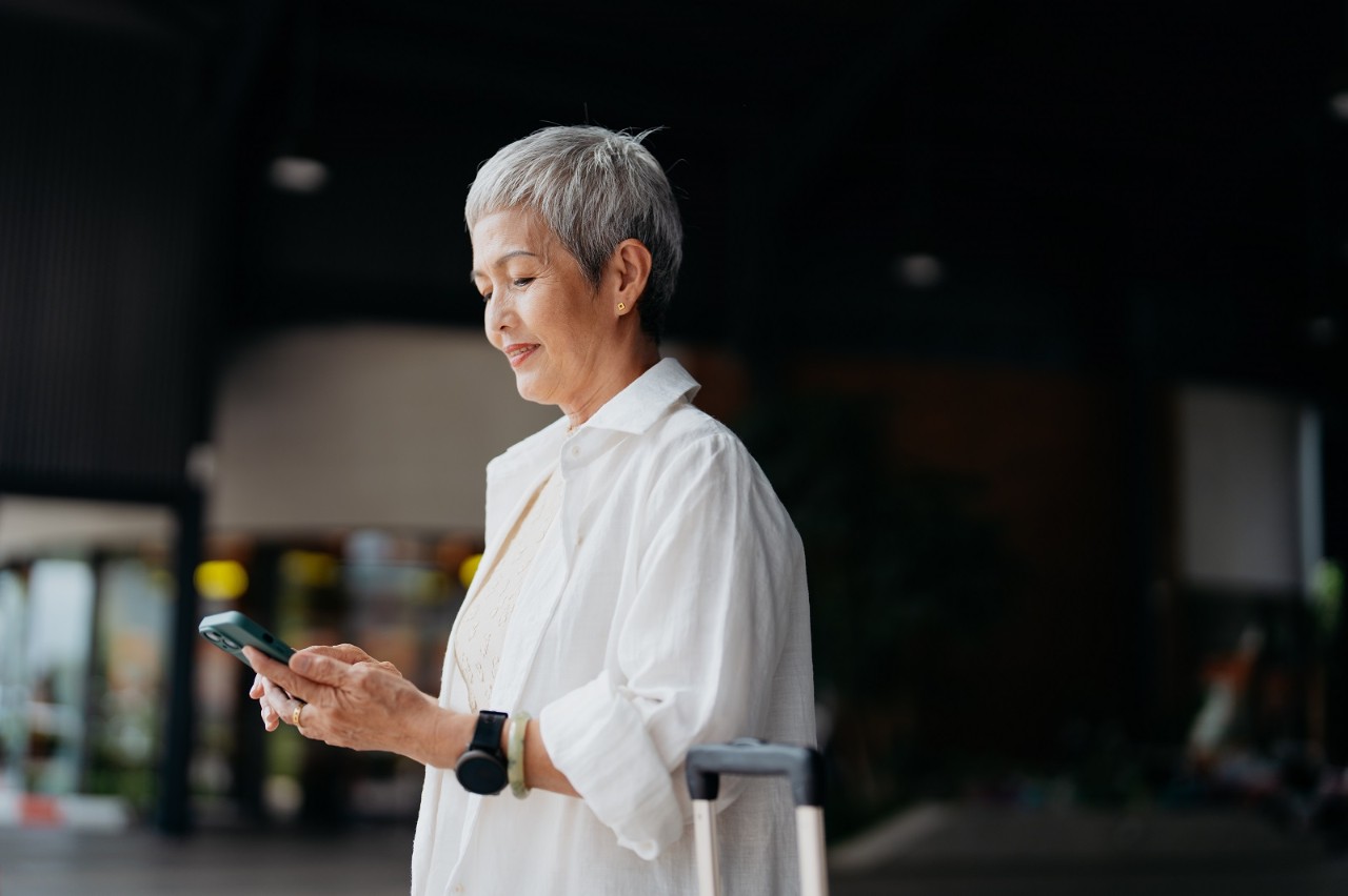 An Asian Chinese businesswoman with luggage using smartphone to order a ride during her trip